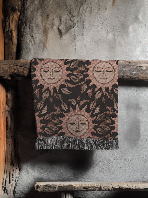 Luxurious woven cotton throw featuring dreamy blush pink sun faces with closed eyes against black background with delicate ray patterns and elegant fringe trim. Perfect celestial wall hanging, witchy bedroom decor, or dark academia throw blanket.